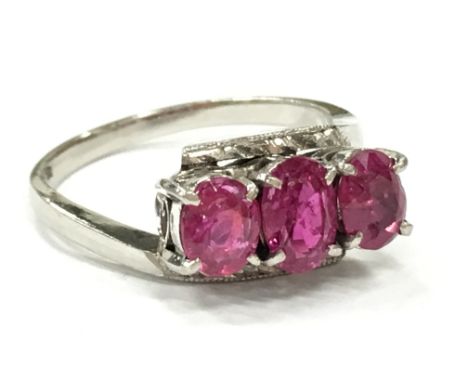 A white metal (possibly platinum) three stone ruby ring.