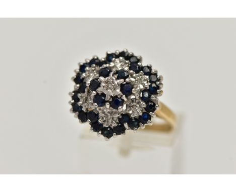 A 9CT GOLD CLUSTER RING, seven single cut diamonds set with thirty circular cut blue sapphires, leading onto a yellow gold sh