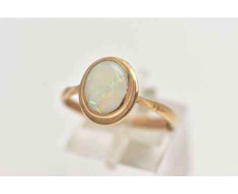 A 9CT GOLD OPAL RING, designed with an oval opal cabochon, collet set to the yellow gold rim, pinched shoulders leading onto 