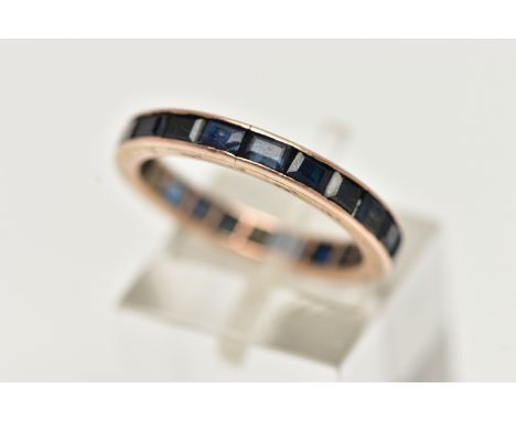 A ROSE METAL FULL ETERNITY RING, set with a full row of square cut deep blue sapphires, channel set in a rose metal mount, un