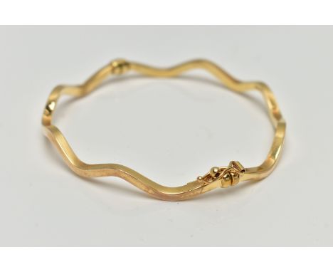 A YELLOW METAL HINGED BANGLE, wave design, hollow hinged bangle, fitted with an integrated and safety clasp, stamped 9kt Ital