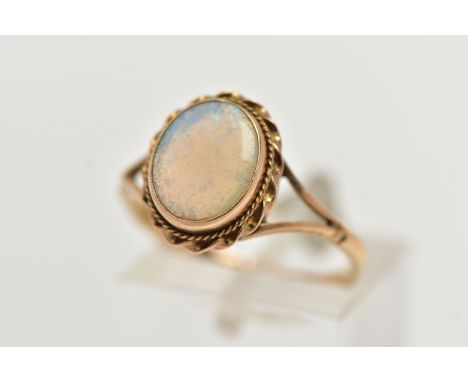 A 9CT GOLD OPAL RING, designed with an opal cabochon, in a milgrain collet setting, to a rope twist surround, bifurcated shou