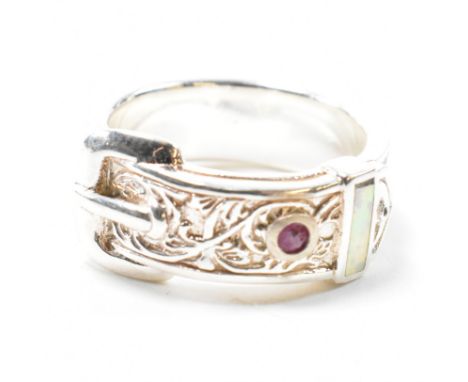 A silver, ruby and synthetic opal buckle ring. The ring in the form of a belt buckle having scrolling decoration set with a r