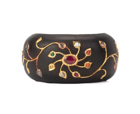 AN INDIAN GEM INSET WOOD BANGLE
The ebonised wood bangle with foliate gold coloured inlay, and set with multi-coloured stones