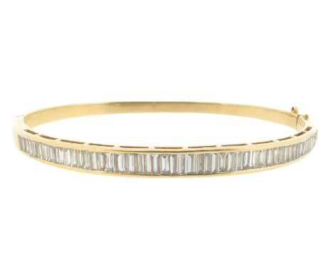 A diamond-set gold bangle, set with a line of baguette-shaped diamonds in yellow gold. 6cm wide (interior).