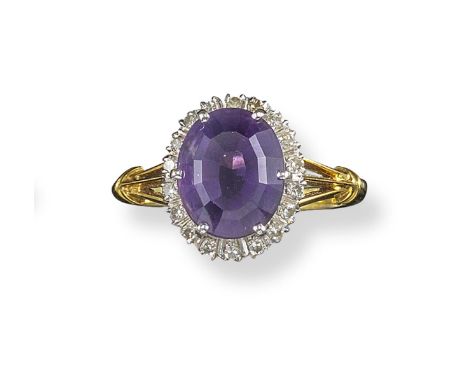 An amethyst and diamond cluster ring, the oval-shaped amethyst is set within a surround of small diamonds in platinum and yel