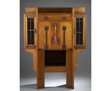 An Arts and Crafts oak desk. 19th/20th century. Strap-hinge drop front desk flanked with glazed door cases. Desk interior has