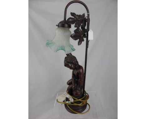 A table lamp in the form of  bronzed resin figure of a young boy sitting on a rock, the lamp having a tiffany style shade.