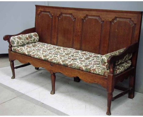 A George III oak four panel settle, straight back with fielded panels, open swept arms with scroll terminals, three turned le