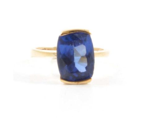 A tanzanite solitaire ring, the rectangular cushion cut stone set to top and bottom in an all yellow metal mount ring size O,
