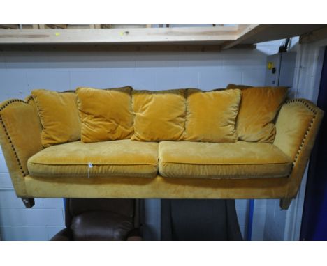 A GOLD VELOUR UPHOLSTERED SOFA, with a studded back, sides, and a shaped top, on square light oak legs, with five scatter cus