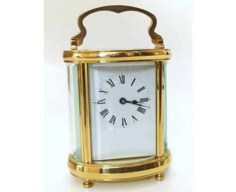 An oval section brass framed carriage clock, with curved bevelled glass panels. The white enamel face has Roman numerals. Eig