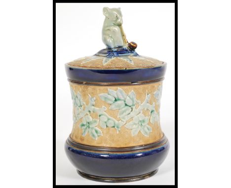 George Tinworth for Doulton Lambeth, a late 19th century lidded stoneware tobacco jar, decorated in relief, the lid with styl