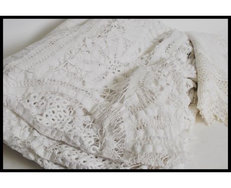 A vintage early 20th century square white linen table cloth with extensive crochet detailing with a linen bed spread having e