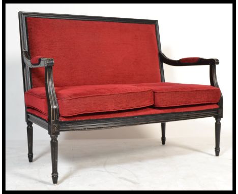 A vintage 20th Century French Louis style ebonised frame conversation Canape sofa settee being upholstered in a rich red fabr