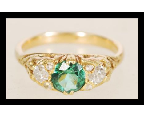 A gold ring with a central green tourmaline stone in decorative floral settings flanked by two 20 pts diamonds. Item weight 4