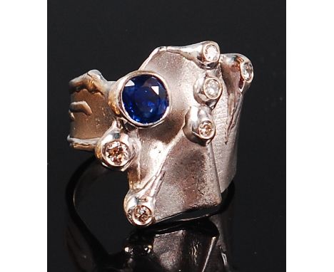 A modern Arts & Crafts 18ct white gold, sapphire and diamond ring, the abstract setting with a round cut sapphire weighing ap