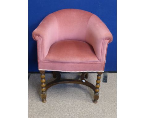 An Oak Framed Boudoir Tub Chair covered in pink velour, the front legs having bobbin style decoration united by shaped stretc
