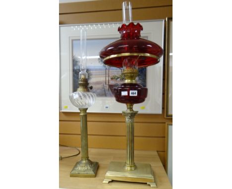 Two oil lamps - one with Corinthian Romanesque column base on a rectangular stand with ruby glass reservoir and shade, the ot