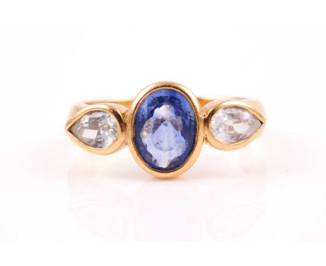 A yellow metal and sapphire ring, rubover-set mixed oval-cut blue sapphire, flanked with two rubover-set mixed pear-cut white