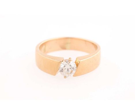 A single stone diamond ring. the round brilliant cut diamond set between a wide yellow metal band cut on a slant. Diamond est