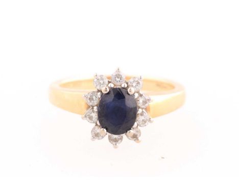 A sapphire and diamond cluster ring; the oval cut sapphire within a border of round brilliant cut diamonds, claw mounts throu