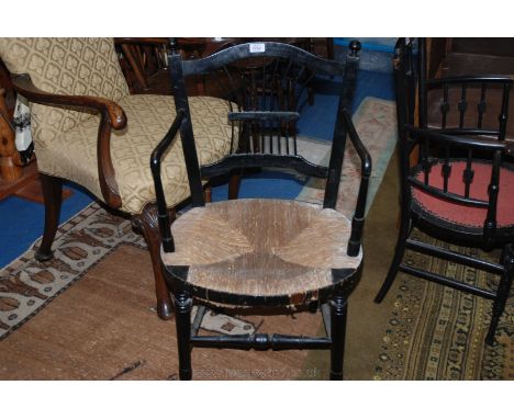 An arts and crafts ebonised rush seated Elbow Chair, having arched top rail, stick back splat with shaped arms, oval rush sea
