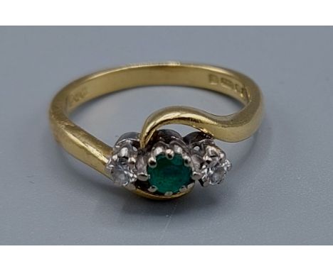 An 18ct gold Emerald and Diamond three stone ring with crossover setting, ring size K, 3.7gms 