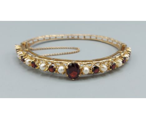 A 9ct gold garnet and pearl set hinged bangle, with nine garnets interspersed with pearls and with engraved decoration, 15.7g