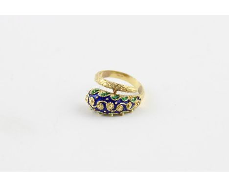 An yellow metal and enamel ring, fashioned as a stylised snake with raised filigree work and champleve blue and green enamel 