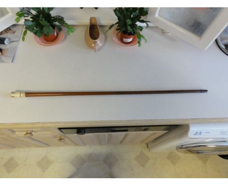 This is a slim cane of polished hard wood. The handle is of bone with crudely carved decoration and an English shilling (Geor