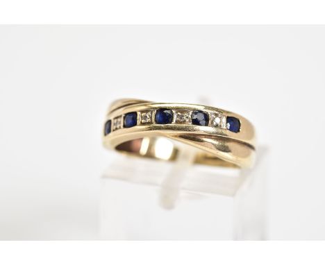 A 9CT GOLD CROSS OVER RING, set with a diagonal row of circular cut sapphire interspaced with round brilliant cut diamonds, w