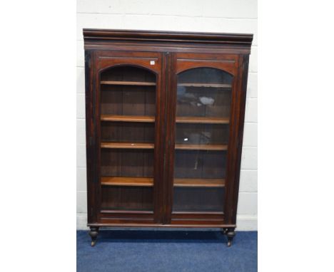 AN EDWARDIAN MAHOGANY DOUBLE DOOR BOOKCASE on turned legs with ceramic casters, width 130cm x depth 33cm xheight 182cm (alter
