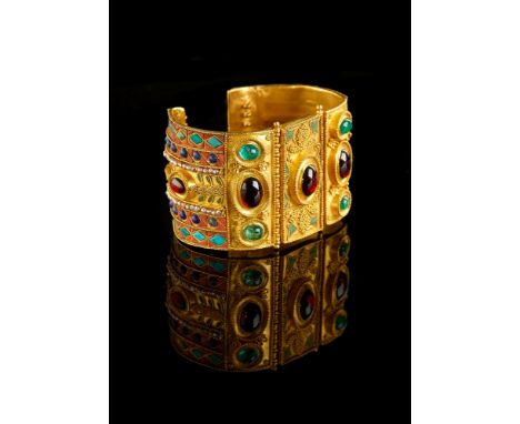 ϒA gold coloured multi gem set bangle by Natalia Josca, the central double hinged panel set with an oval cabochon garnet in a
