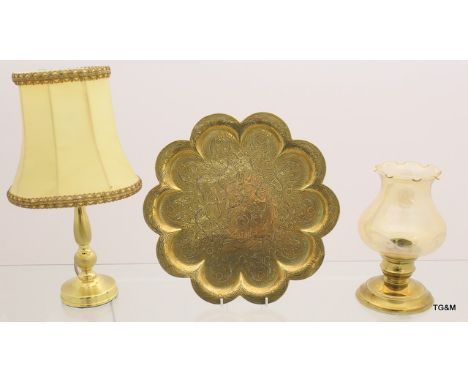 A small brass charger, brass lamp and brass candle stick holder