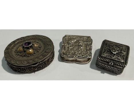 A silver shaped square patch box, decorated in relief with putto, 2.5cm wide, marked 925; other silver pill or patch boxes, e