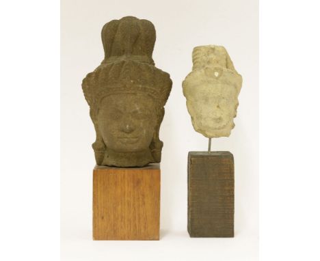 Two stone carvings of heads of a bodhisattva, Cambodian, each wearing a tall hat with jewels, fitted on a wood pedestal, 23 a