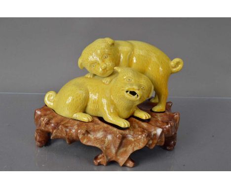 A Chinese yellow glazed porcelain sculpture group of dogs playing, Qing Dynasty on a later carved hardwood base. Provenance: 