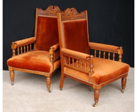 Pair of late Victorian oak armchairs, each with floral scroll pediment over cushioned back, seat and open arms, on baluster t