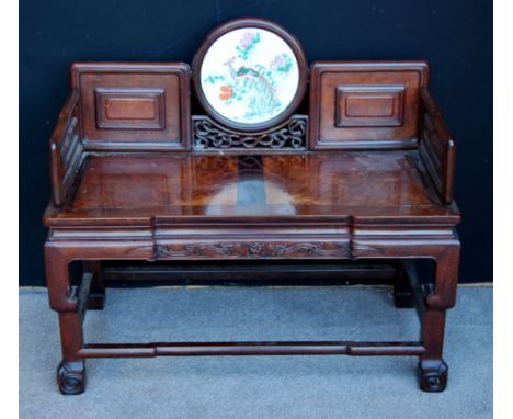 Chinese two-seater wooden sofa with walnut inlay to seat, carved frieze and circular inset porcelain panel to the back, on sc