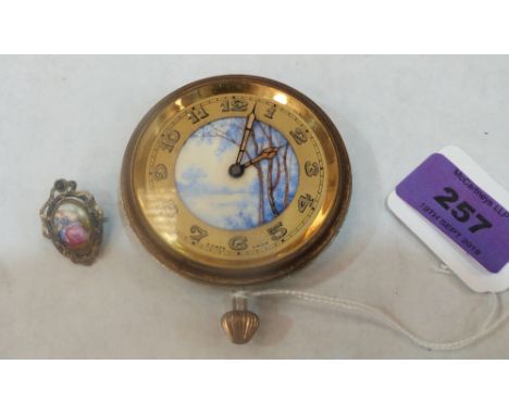 A 1920s Swiss travelling clock with painted dial, movement runs, together with a base metal and ceramic pendant