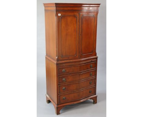 A reproduction mahogany serpentine-front tall cabinet the upper part fitted shelf enclosed by a pair of panel doors, the base