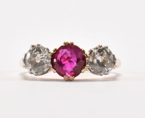 An 18ct gold ruby and diamond three stone ring. The ring being set with a round cut ruby to the centre flanked by to round cu