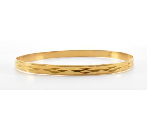 A gold bangle bracelet. The bracelet of round form with incised decoration to the sides. Marked 750 to the interior of the ba