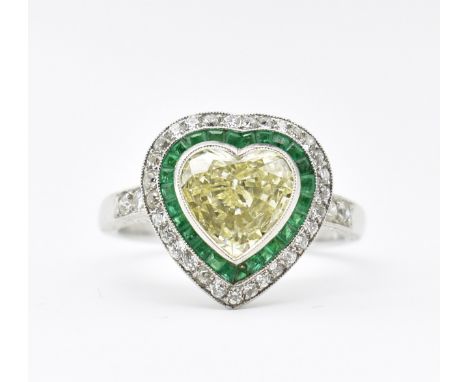 An Art Deco style emerald and diamond target ring. The ring having a principal heart shaped yellow diamond surrounded by cali