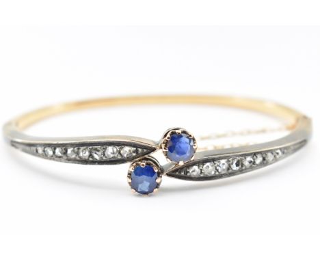 A French 18ct gold and silver sapphire and diamond bangle. The bangle set with two mixed cut sapphires in a crossover setting