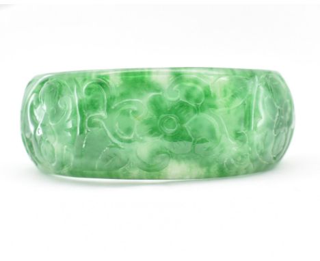 A Chinese carved green stone bangle. The bangle carved with bat fruit and floral figures. Diameter 7cm. Circumference approx 