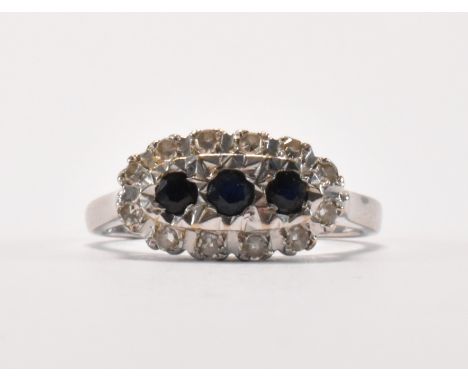 A hallmarked 18ct white gold, sapphire and diamond ring. The ring being set with three round cut sapphires surrounded by roun