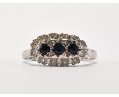 A hallmarked 18ct white gold, sapphire and diamond ring. The ring being set with three round cut sapphires surrounded by roun