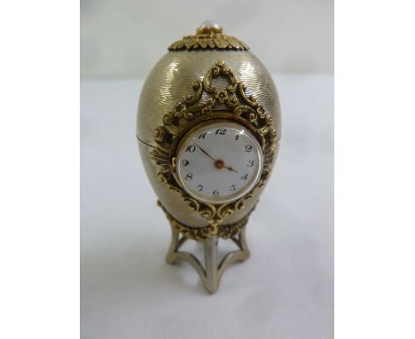 An engine turned silver Easter Egg desk clock with silver gilt mounts on integrated stand and pearl finial, London 1983